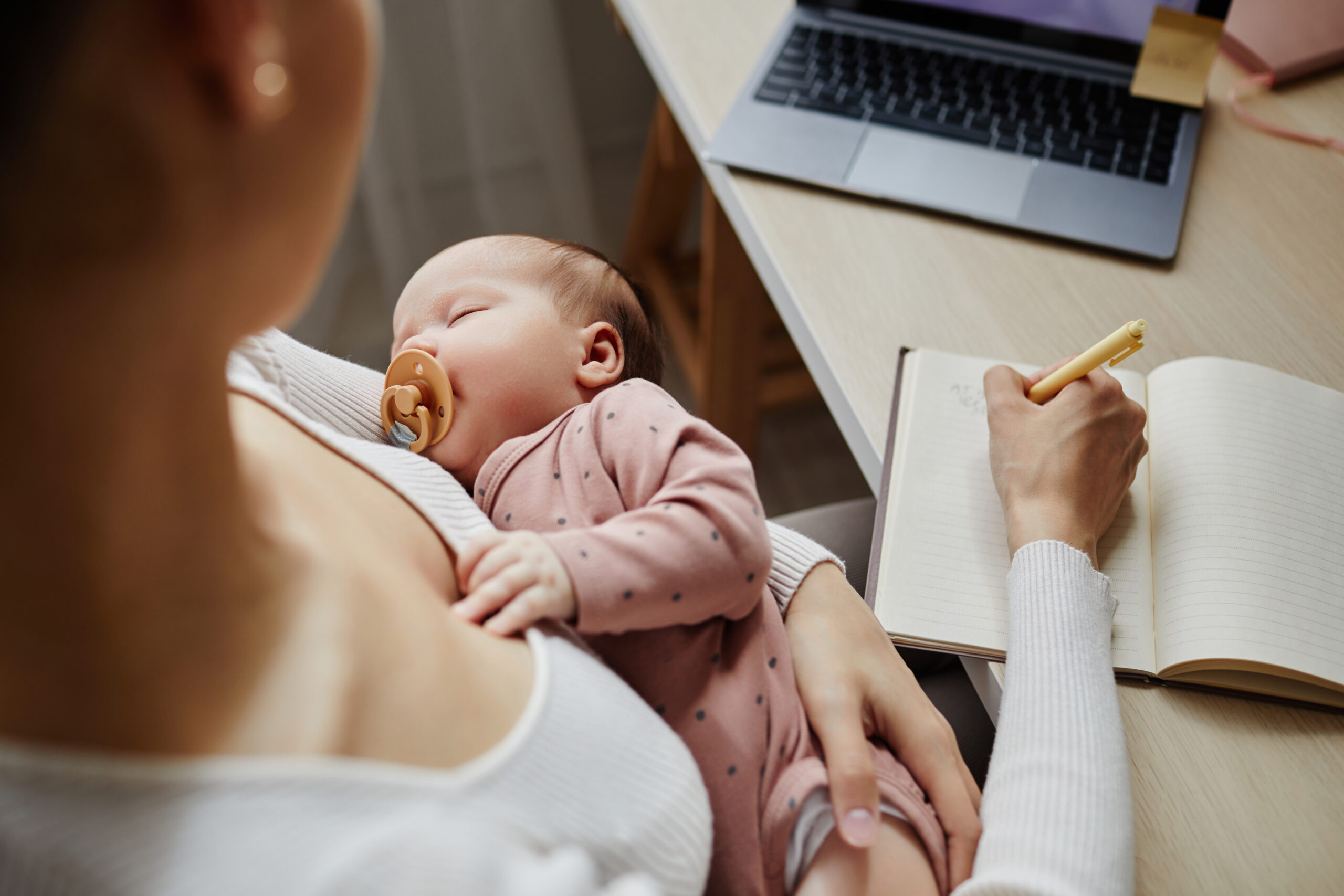 femme ecrivant dans un carnet tout en portant son bébé